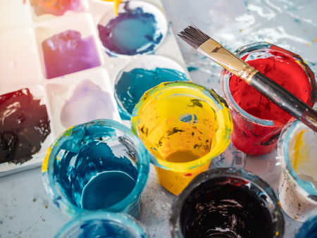 Acrylic colour in plastic cups with paintbrush and colorful artist palette on dirty paints background in art studio.の写真素材