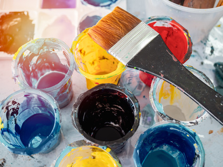 Acrylic colour in plastic cups with paintbrush and colorful artist palette on dirty paints background in art studio.の写真素材
