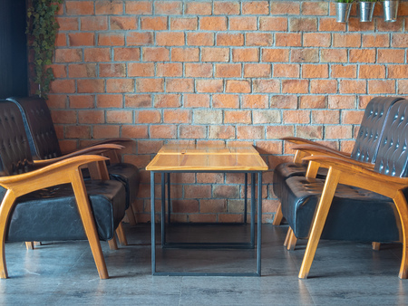 Black vintage leather wooden sofa and wooden table on brick wall background in loft style cafe.の写真素材