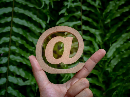 Wooden E-mail address symbol on correct pointing hand sign, arroba icon on green leaves background with. E-mail marketing online internet, technology and environment concept.の写真素材