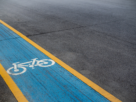 Bike lane. White bicycle icon on blue and yellow background on the old road with copy space.の写真素材