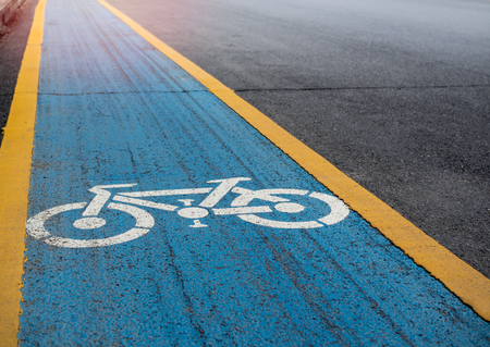 Bike lane. White bicycle icon on blue and yellow background on the old road with copy space.の写真素材