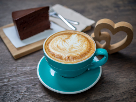 Coffee latte art in blue cup with a piece of chocolate cake, forks and wooden heart on wooden table background. Coffee lover concept.の写真素材