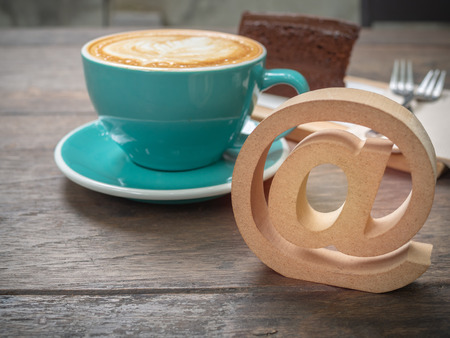 Coffee latte art in blue cup with wooden arroba symbol or email address icon on wooden table background with space. Coffee lover and social network business concept.の写真素材