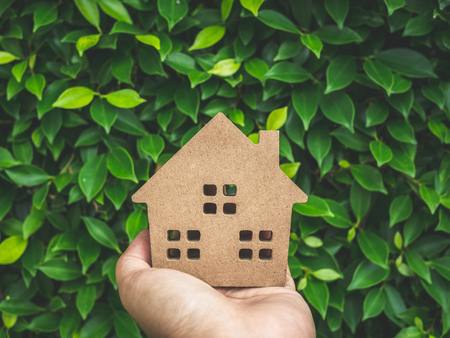 Wooden house on left hand on green leaves background. Home ecology concept.の写真素材