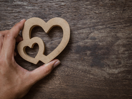 Hand with wooden twin hearts on old wooden texture background with copy space. Love concept.の写真素材
