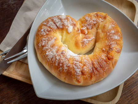 Sweet baked bread on top with sugar on white plate with knife, fork o wooden tray on wooden table background on top view.の写真素材