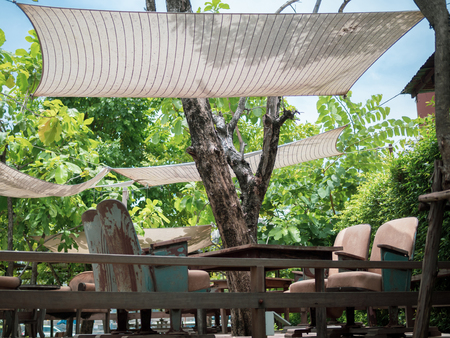 Vintage theatre seats with wooden table on wooden terrace with fabric roof on green tree and blue sky background. Unique mix and match furniture style concept.の写真素材
