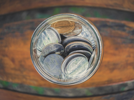 Close up coins in glass jar top view on wooden table background in fish eye lens style. Saving money...