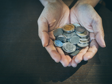Coins in hands on wooden table background. Saving money and donation concept.の写真素材