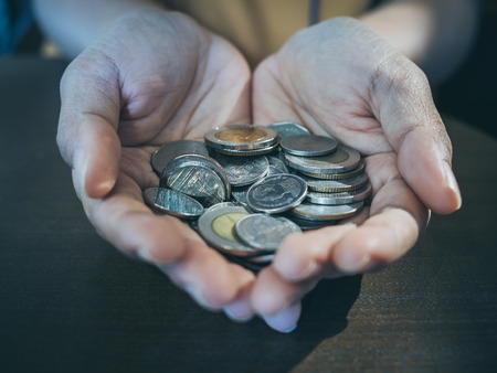 Close up coins in hands on wooden table background. Saving money and donation concept.