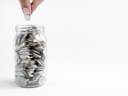 Hand holding coin in glass jar isolated on white background with copy space. Saving money concept.の写真素材