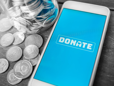 Close-up donate icon button on blue screen on white mobile phone with coins Thai baht money on...