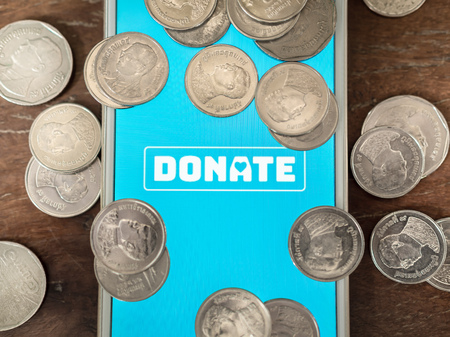 Flat lay donate icon button on blue screen on white mobile phone with coins Thai baht money on wooden background with copy space. Donation online concept.の写真素材