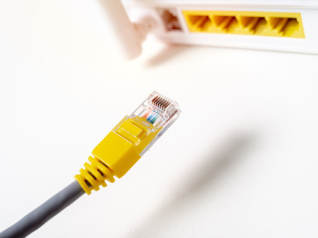 Close-up yellow ethernet cable connecting on white wireless internet WI-FI router network hub...