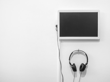 Blank monitor and headphone hanging on clean white wall with copy space.