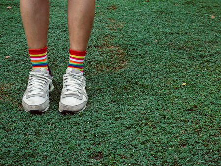 Legs wearing colorful stylish socks and white sneakers on green field hipster style with copy space.の写真素材