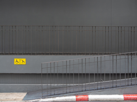 Wheelchair and stroller yellow sign and on the wall and ramp near the street on building background.