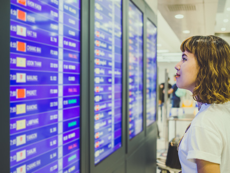 Asian woman short hair wearing white shirt checking flight at the flight information board in...