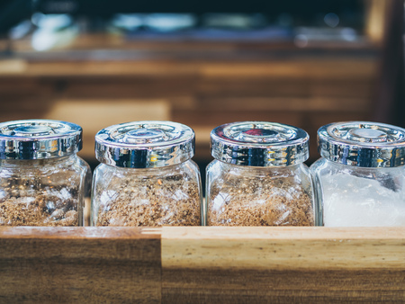 Set of glass bottle of brown sugar and white sugar on wooden shelf in cafe.