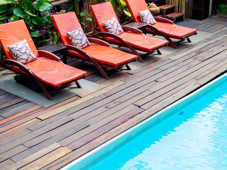 Row of vintage wooden sunbed with orange pad and pillow near the swimming pool.