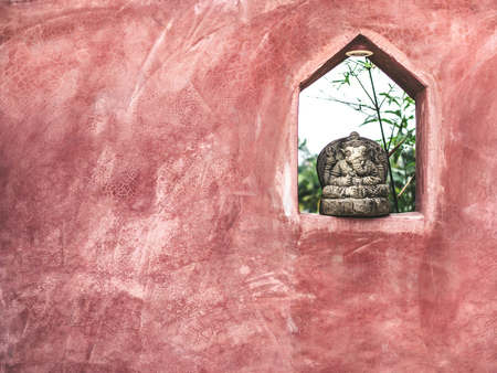 Small sitting Ganesha stone sculpture decoration on the space on grunge red cement wall with copy space.の写真素材