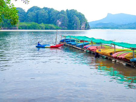 KRABI, THAILAND - November 2, 2018: Local men take the colorful fiberglass kayaks to the outdoor storage on seascape and mountain background in Krabi, Thailand.の写真素材