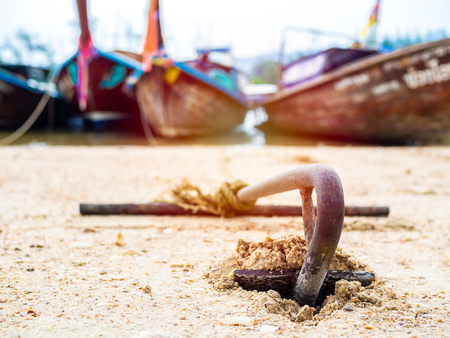 Rusty anchor on the sand beach with traditional long tail boat on the sea in Thailand.の写真素材