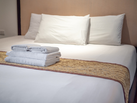 Clean white towels and three white pillows on bed in luxury room in hotel.の写真素材