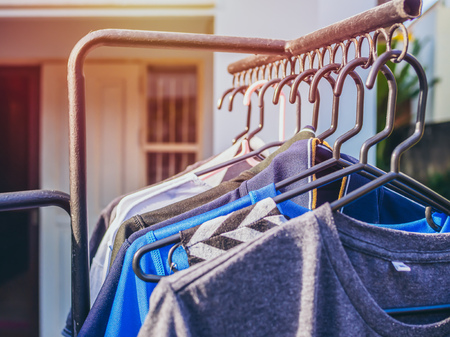 Many colors shirts on hanger are hanging on the clothesline with sunshine.