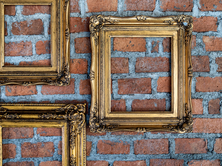 Three empty old ornate golden frames hanging on brick wall.