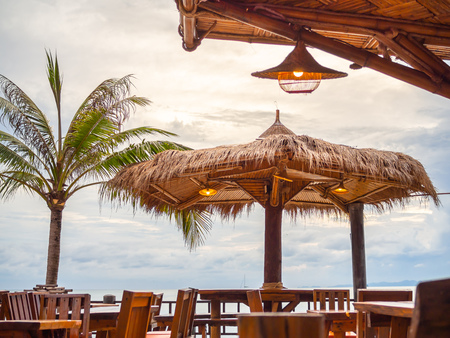 Bamboo hut pavilion with wooden chairs and table in restaurant on seascape background on sunset sky in Thailand.の写真素材