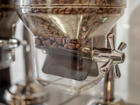 Close-up coffee bean contained in glass tubes with stainless steel clamping hand knob on white wall in coffee shop.の写真素材