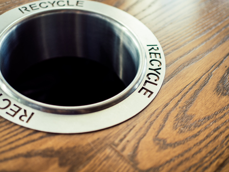 Close-up modern round recycle trash bin hole on wooden background in coffee shop.の写真素材