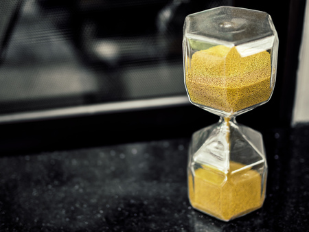 Modern hexagon hourglass with golden sand seed on black table with copy space. Time passing and...