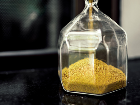 Close-up modern hexagon hourglass with golden sand seed on black table with copy space. Time passing...