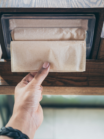 Hand picking brown napkin from the box on wooden tray on wooden table in coffee shop vertical style.の写真素材