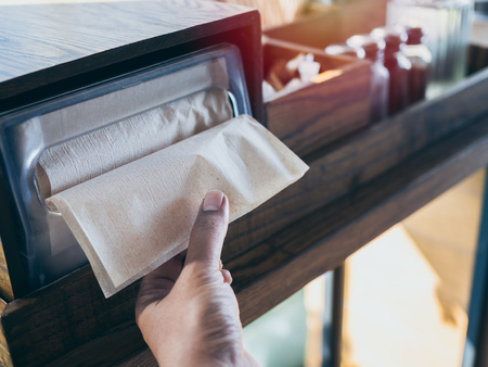Hand picking brown napkin from the box on wooden tray on wooden table in coffee shop.の写真素材