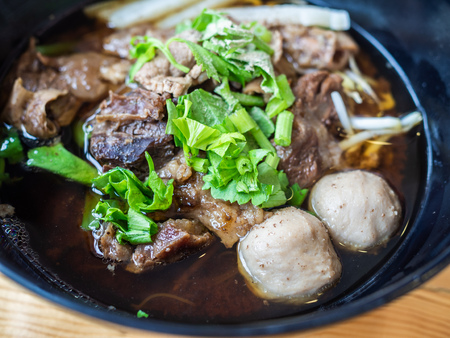 Close up of black bowl of Chinese style beef noodle soup with beef stew, meat balls and fresh cut...