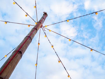 Vintage light bulbs on wire on wooden bamboo pillar on blue sky background. Local festival lighting...