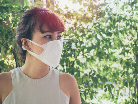 Beautiful asian woman wearing white protective N95 dust mask on green leaves background with copy space. Protection against pollution concept.の写真素材