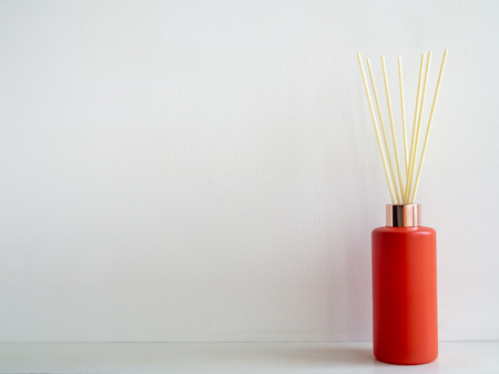 Air freshener stick in red bottle on white wall background with copy space. Aromatic reed stick in...