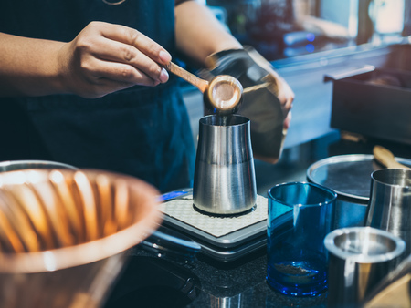 Barista's hand putting ground coffee in stainless steel manual coffee grinder in coffee shop.の写真素材