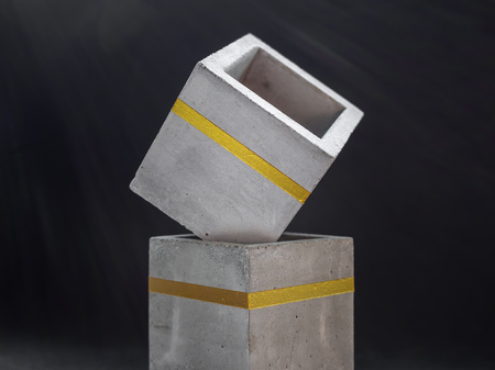Close-up two empty modern cubic concrete planters with gold color bar on dark background. Painted...
