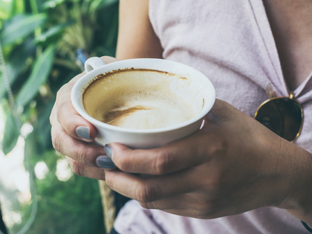 Close-up woman hands holding a white hot coffee cup in cafe with copy space.の写真素材