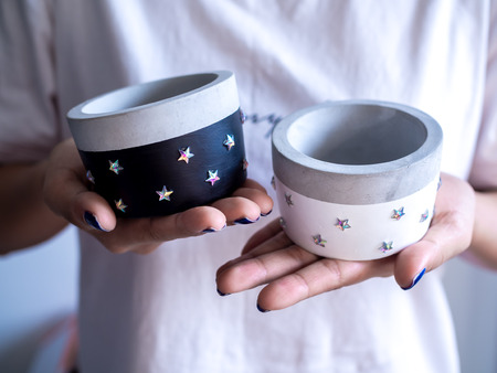 Hands holding empty black and white modern round concrete planters with shining star pattern. Painted concrete pots for home decorationの写真素材