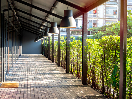 Wooden floor terrace space with ceiling light under the roof near the green garden with beautiful sunlight and shadow.の写真素材
