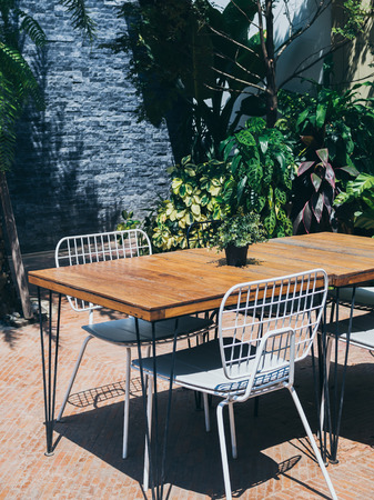 Wooden dining table with white chairs in the outdoor garden on sunny day vertical style.の写真素材
