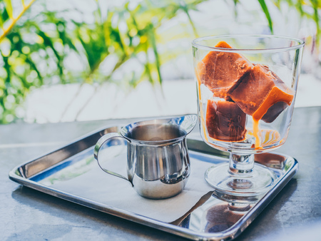 Thai milk tea ice cubes in glass with milk in small jug on stainless steel tray on concrete table.の写真素材