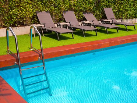 Sunbeds on green grass and grab bars ladder on outdoor swimming pool in the garden with copy space.